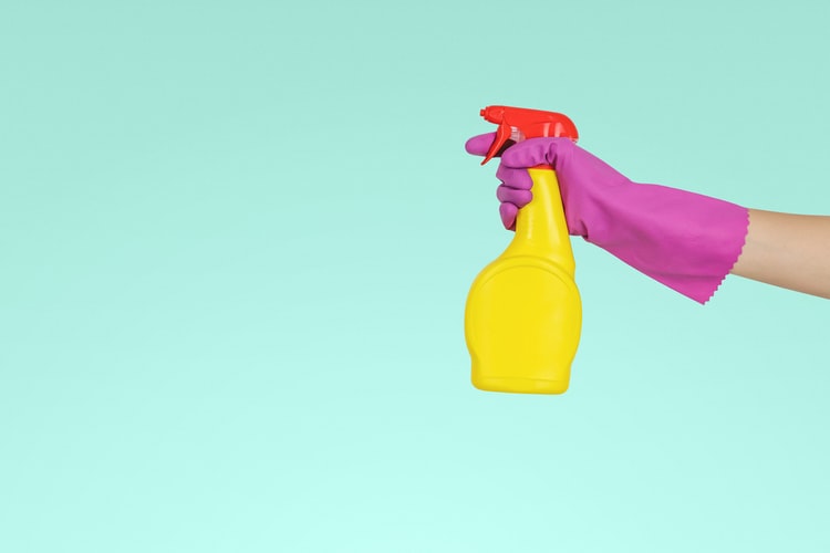 A person holding a spray bottle with a glove on their hand