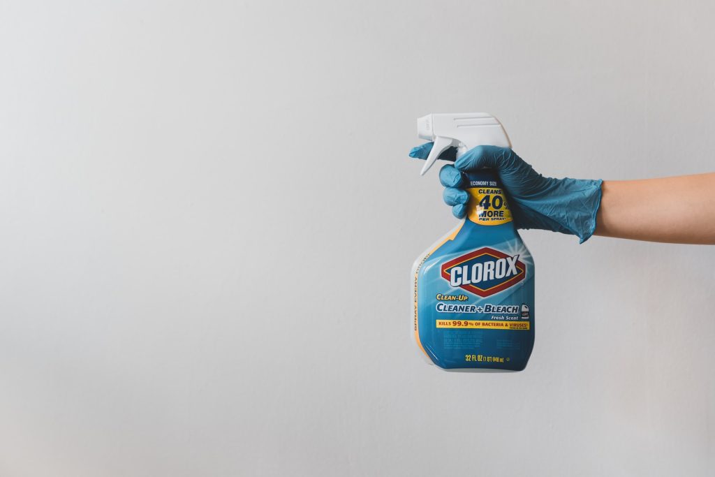 A hand in a blue glove, holding a plastic bottle of disinfectant
