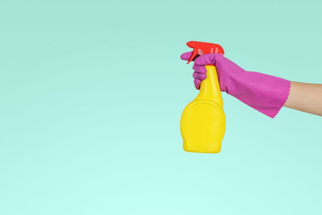 A hand with a rubber glove holding a sanitizer